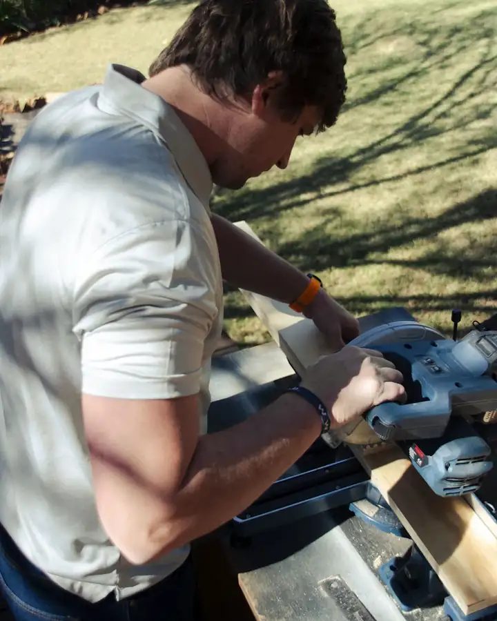Ein Handwerker sägt im Freien ein Brett an einer Kappsäge