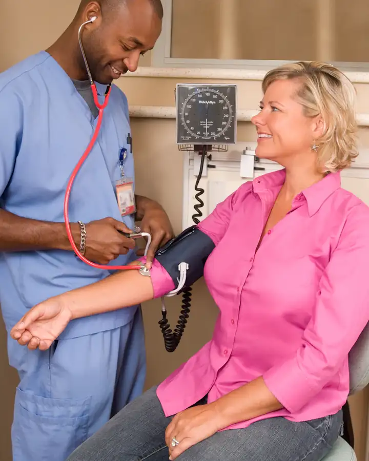 Eine Mitarbeiterin misst in einer Praxis den Blutdruck einer Patientin