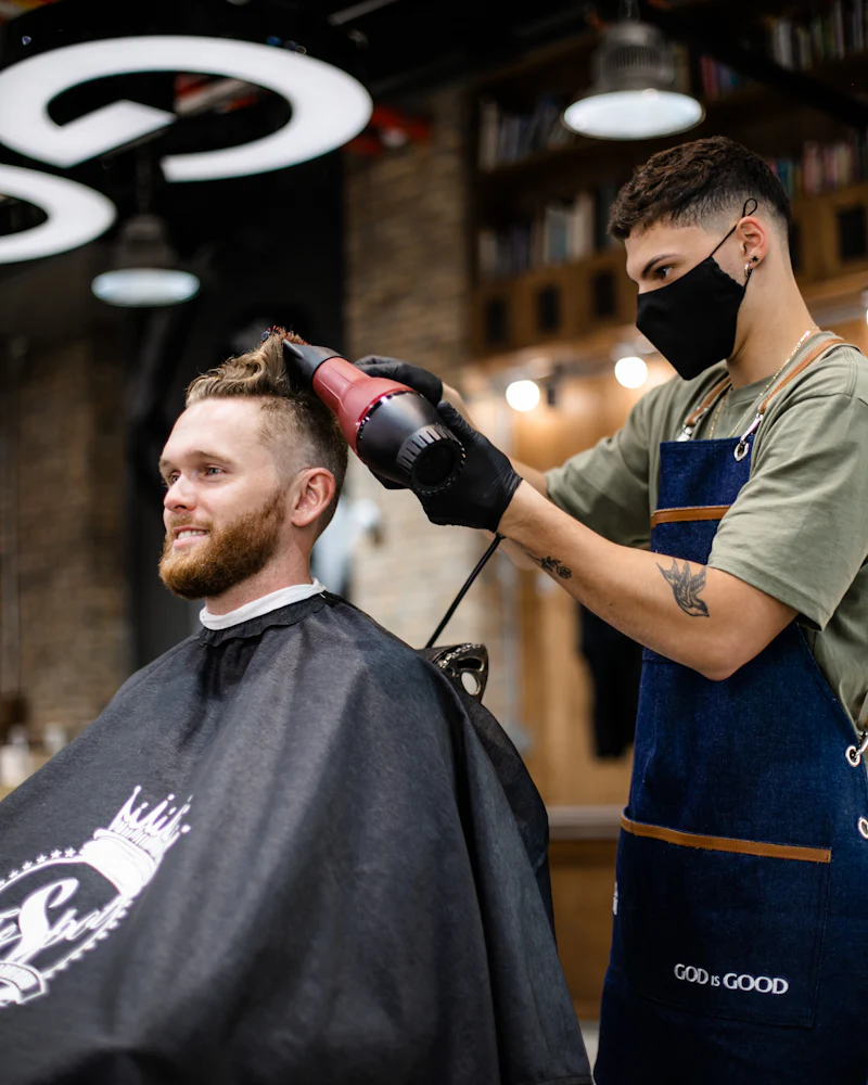 Ein Friseur föhnt einem Kunden im Salon die Haare
